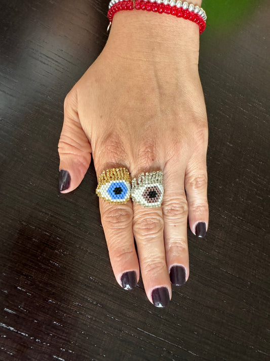 A hand wearing two rings with blue and gold colors, one with a evil eye design 