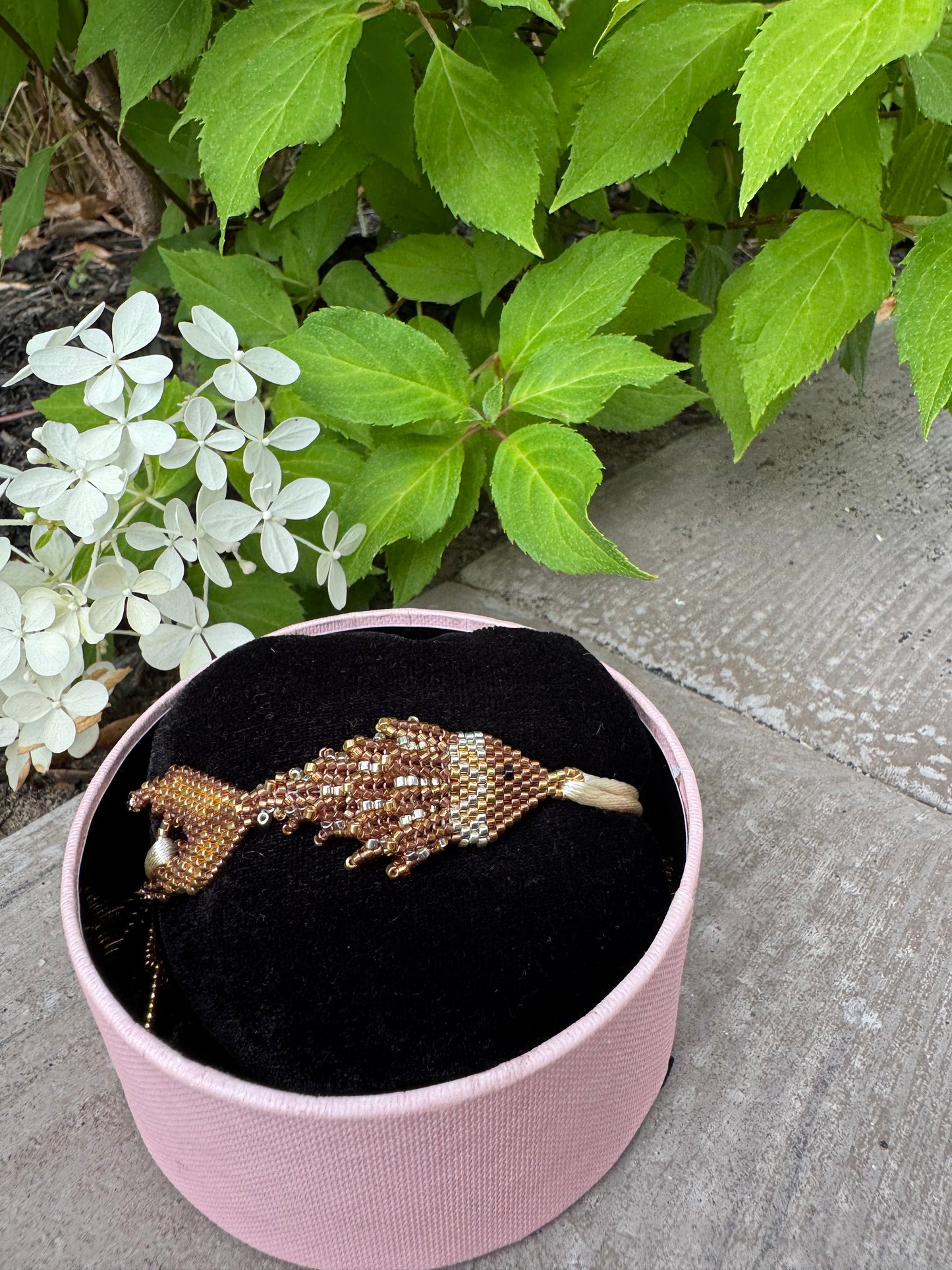 Pink jewelry box with a decorative brooch on a concrete surface with greenery.