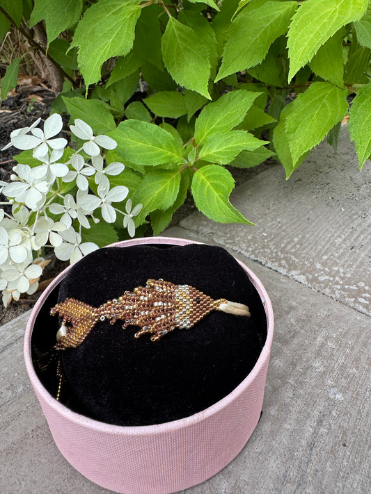 Pink jewelry box with a decorative brooch on a concrete surface with greenery.