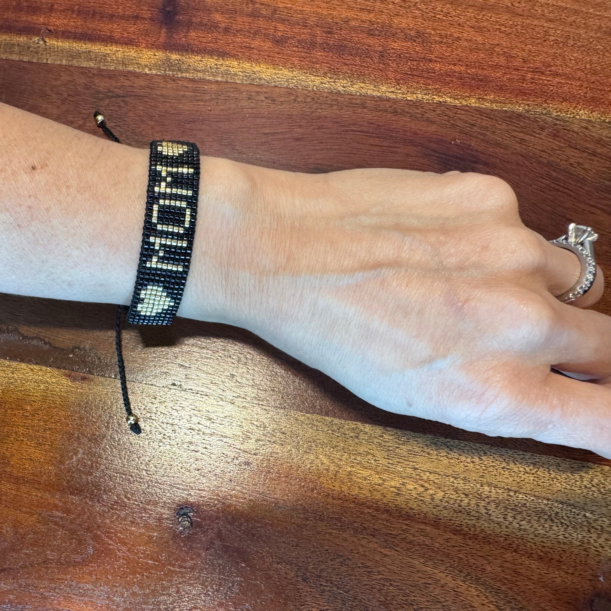 Hand wearing a bracelet with 'MOM' on a wooden surface