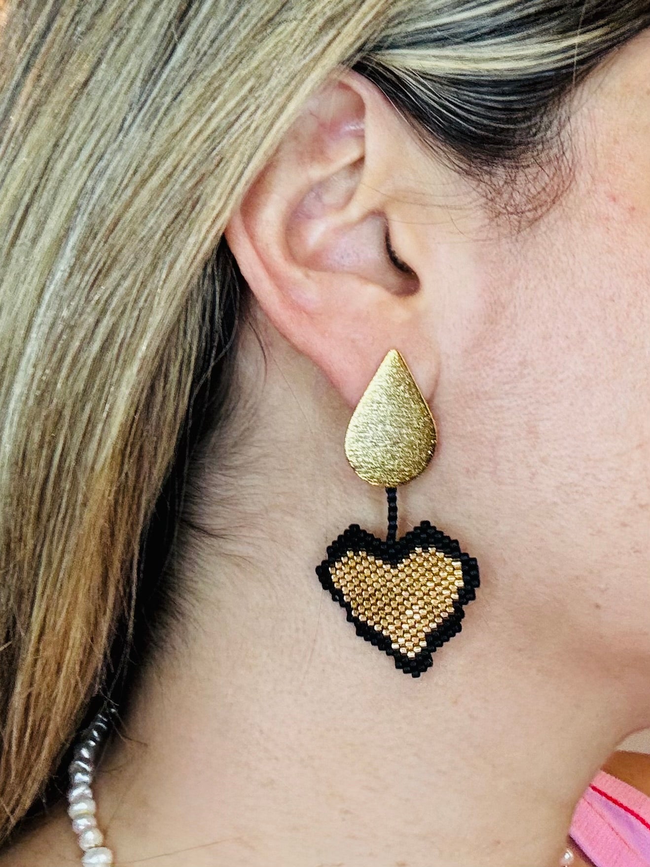 Close-up of a gold teardrop earring with a black heart-shaped pendant.