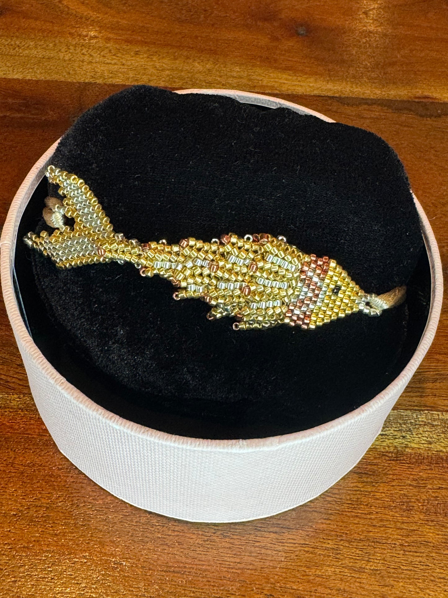 A Pez-shaped bracelet made of multicolored beads, displayed on a round box.
