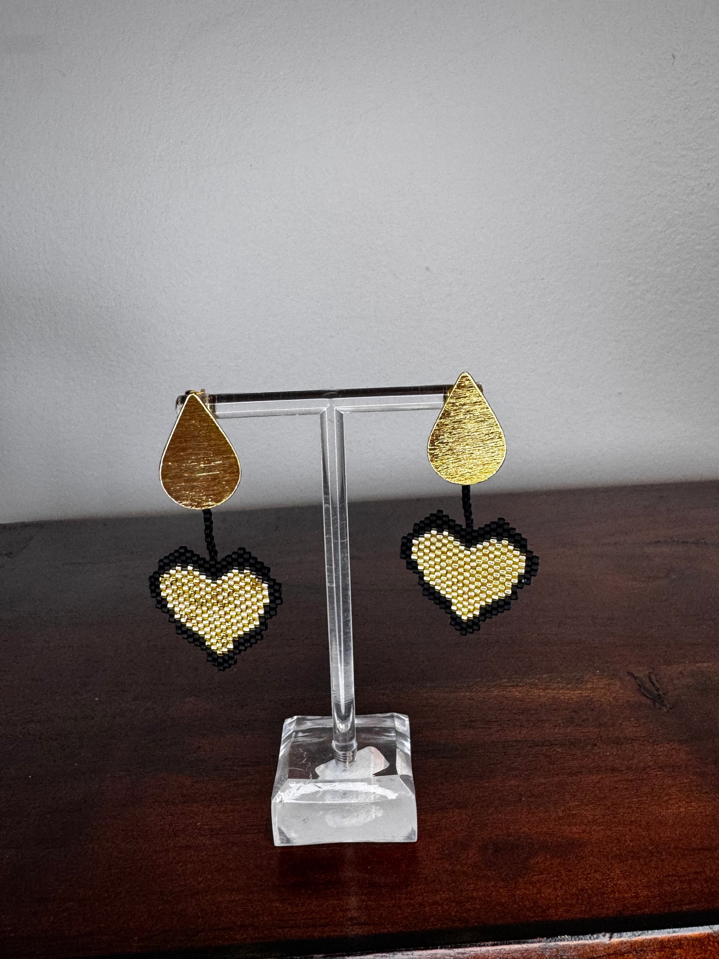 Gold heart-shaped earrings on a clear stand against a neutral background.