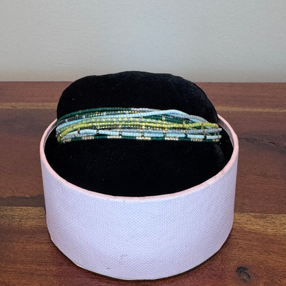 Black beret and green beaded bracelets in a white box on a wooden surface