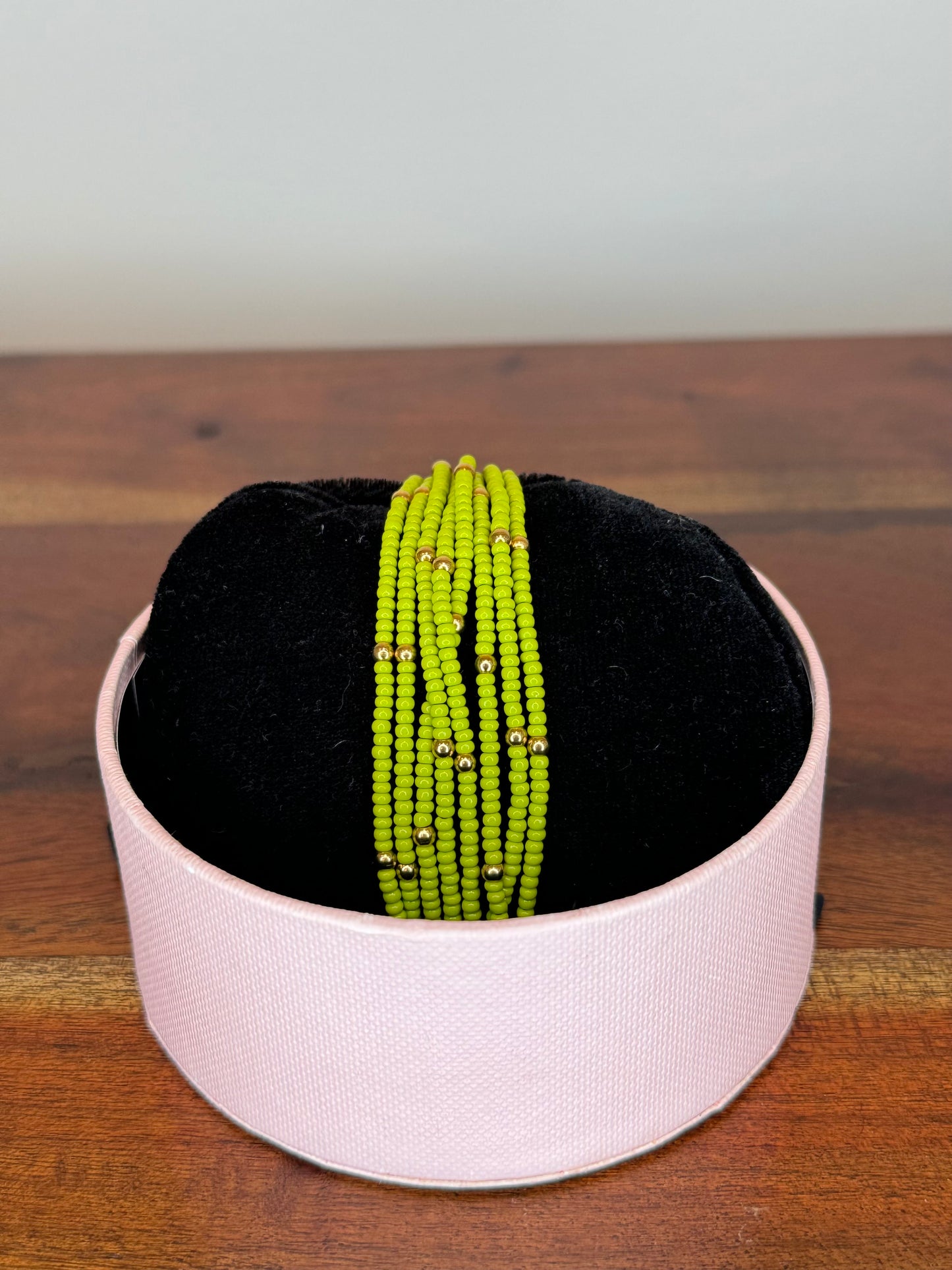 A multi-colored beaded bracelet displayed on a white stand with a black base, set on a wooden surface.
