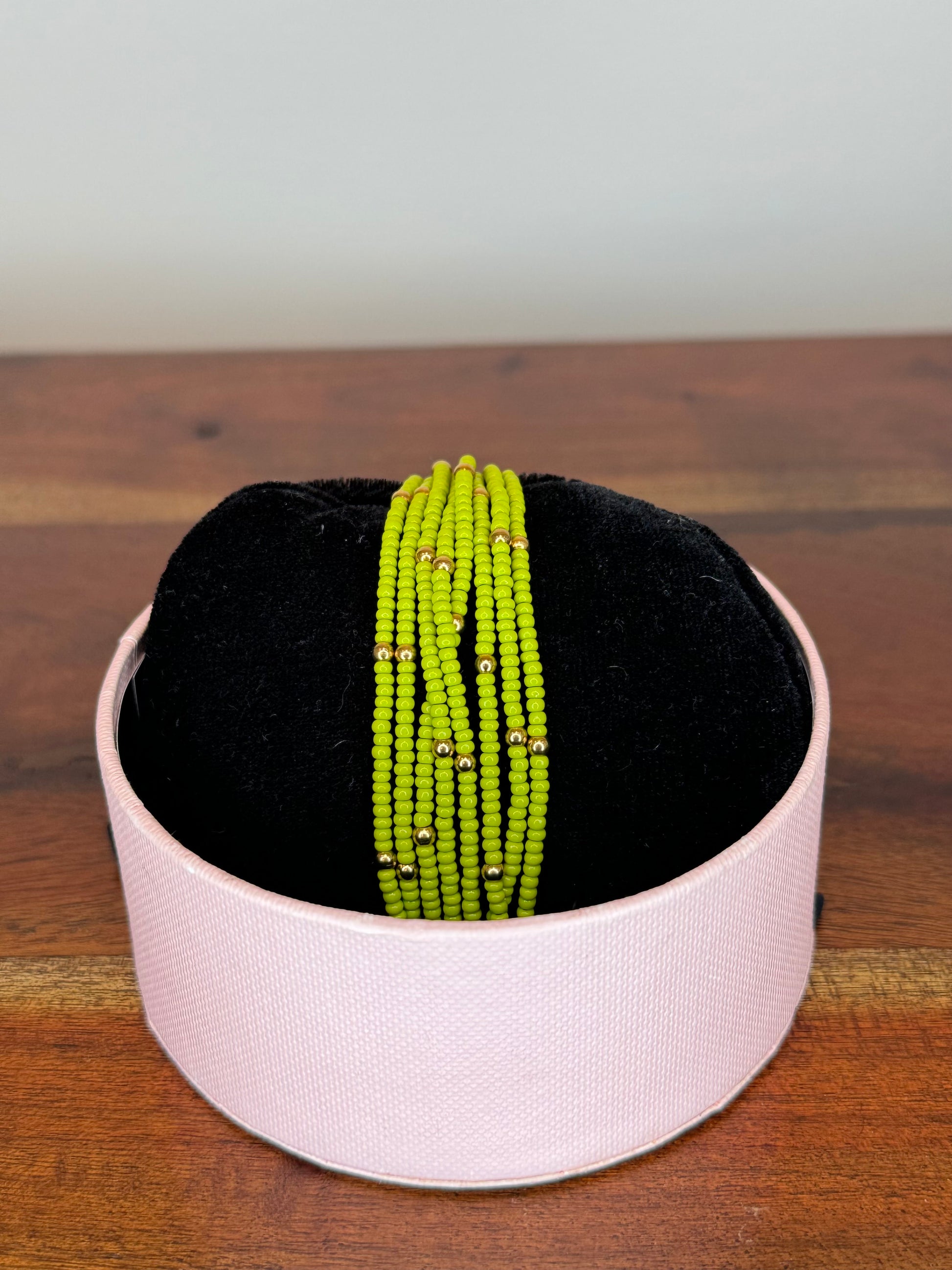 A multi-colored beaded bracelet displayed on a white stand with a black base, set on a wooden surface.
