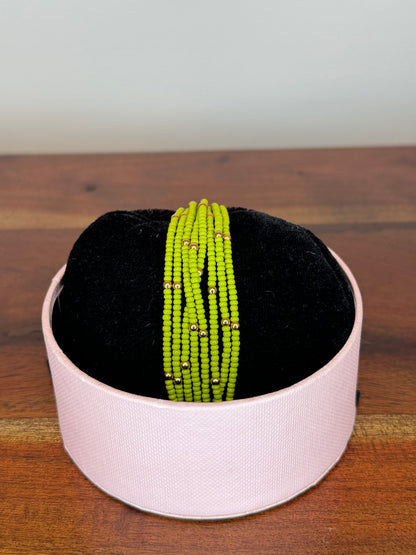 A multi-colored beaded bracelet displayed on a white stand with a black base, set on a wooden surface.