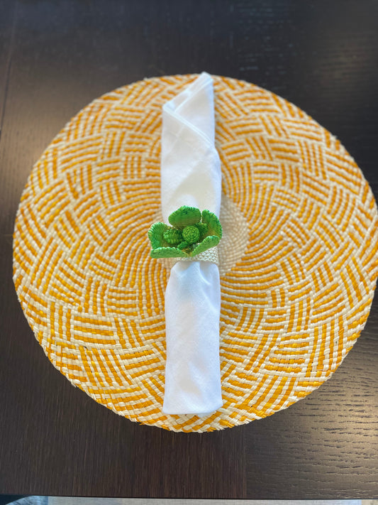 A yellow and green floral patterned napkin ring holding a white napkin, displayed on a dark surface.