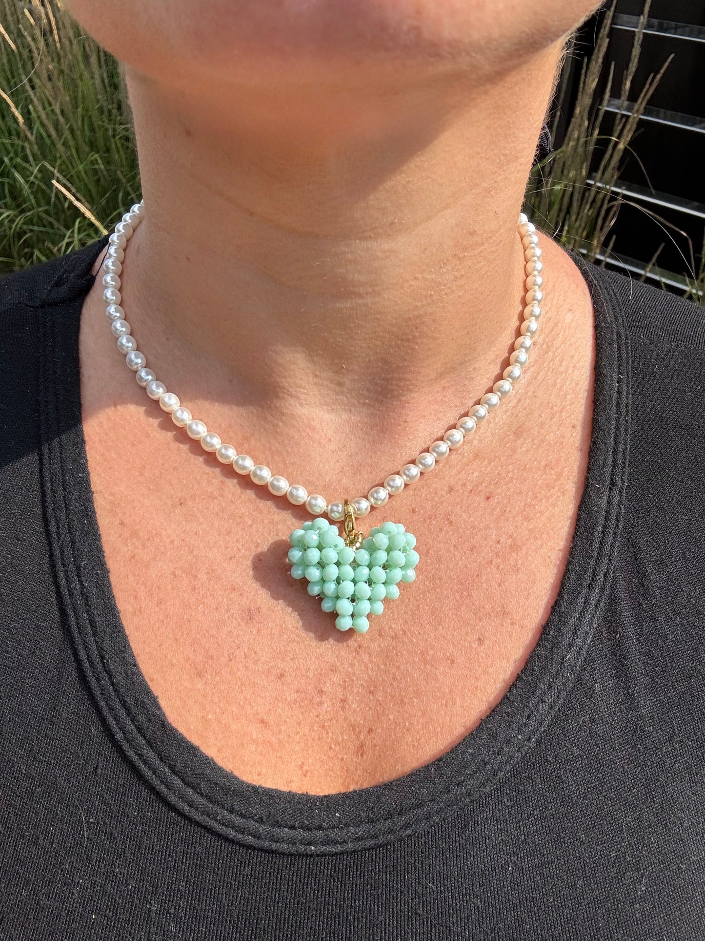 Pearl necklace with a heart-shaped turquoise pendant worn by a person against a natural background.