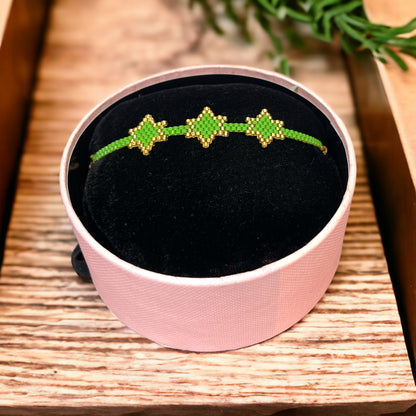 A bracelet with green and gold colors displayed on a black cushion inside a pink box.