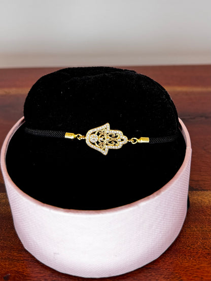 Gold bracelet with a decorative clasp on a black cord