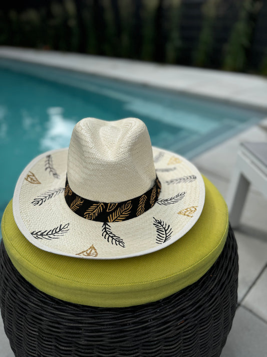A hand-painted Panama hat displayed on a cushioned stool with a pool in the background.