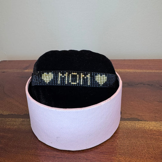 Black beaded bracelet with 'I love mom' text on a white box against a wooden surface.