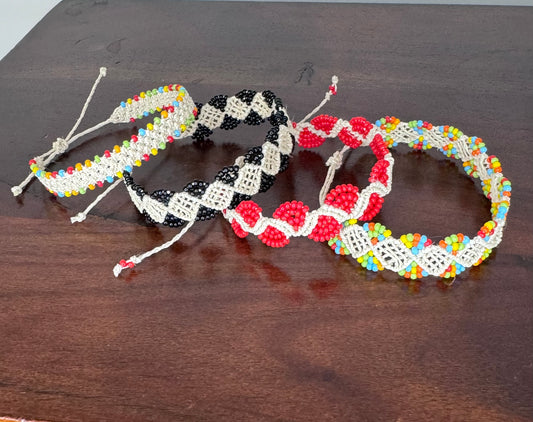 A collection of four handcrafted bracelets with natural fiber and acrylic beads, displayed on a wooden surface. The bracelets feature various patterns and colors.