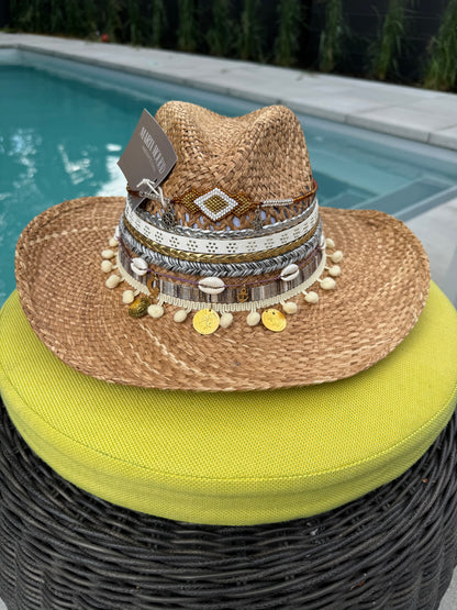 A handwoven straw hat with a geometric rhombus shape decoration, displayed on a cushion beside a pool.