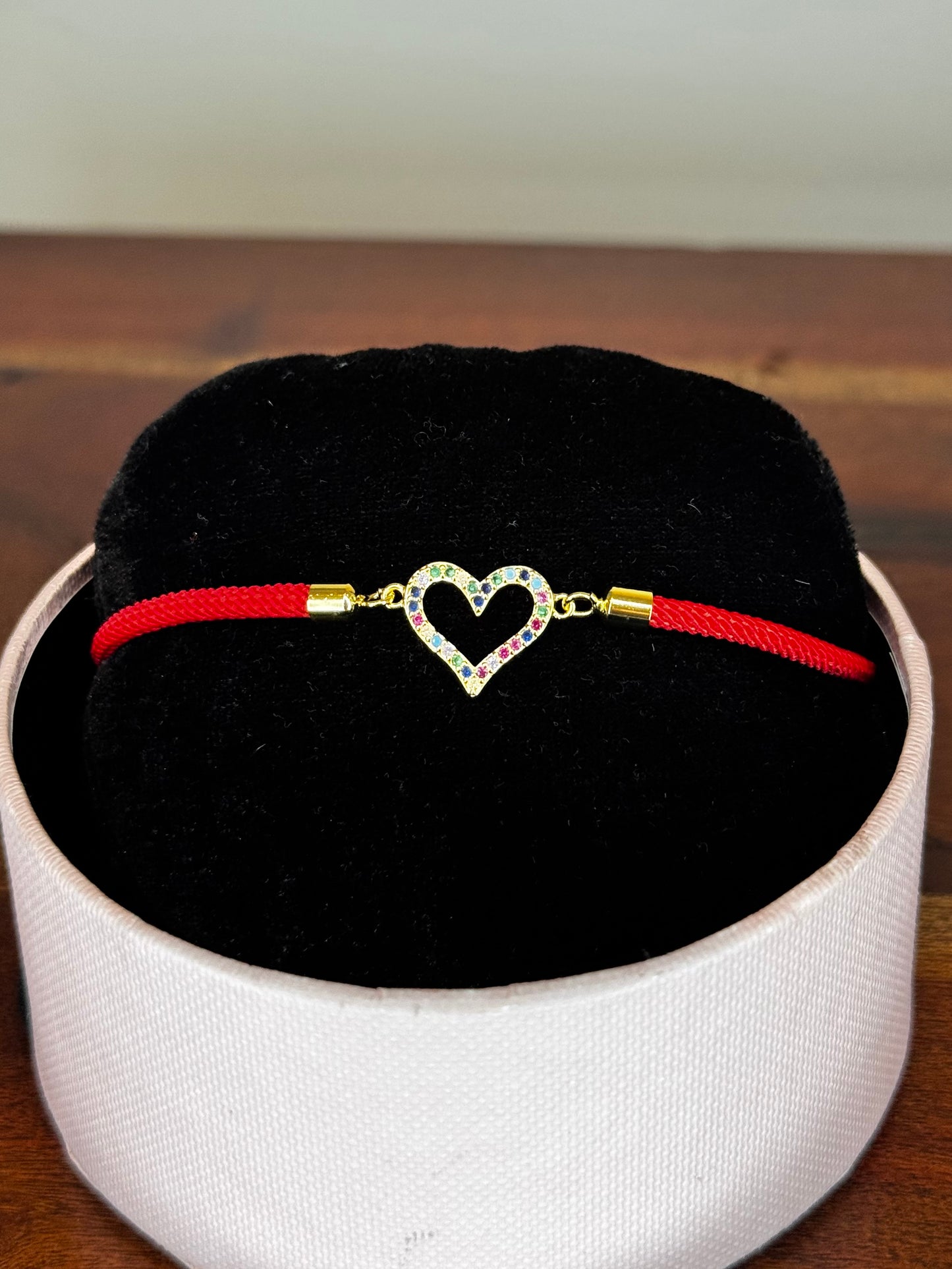 Red bracelet with a heart-shaped clasp on a black cushion inside a white box.