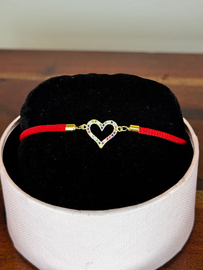 Red bracelet with a heart-shaped clasp on a black cushion inside a white box.