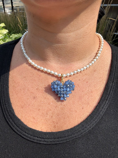 Pearl necklace with a blue heart-shaped pendant worn by a person.
