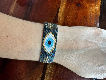 Beaded bracelet with eye design on a wrist against a wooden background