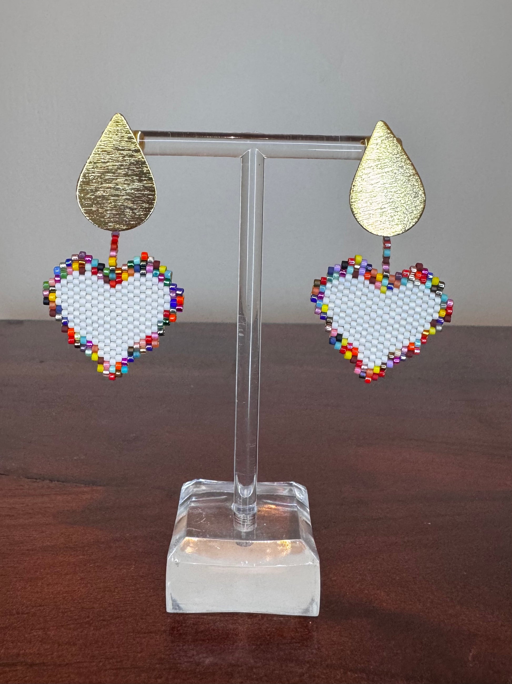 A pair of Miyuki earrings displayed on a stand, featuring a white beaded design with a gold-colored drop-shaped top.