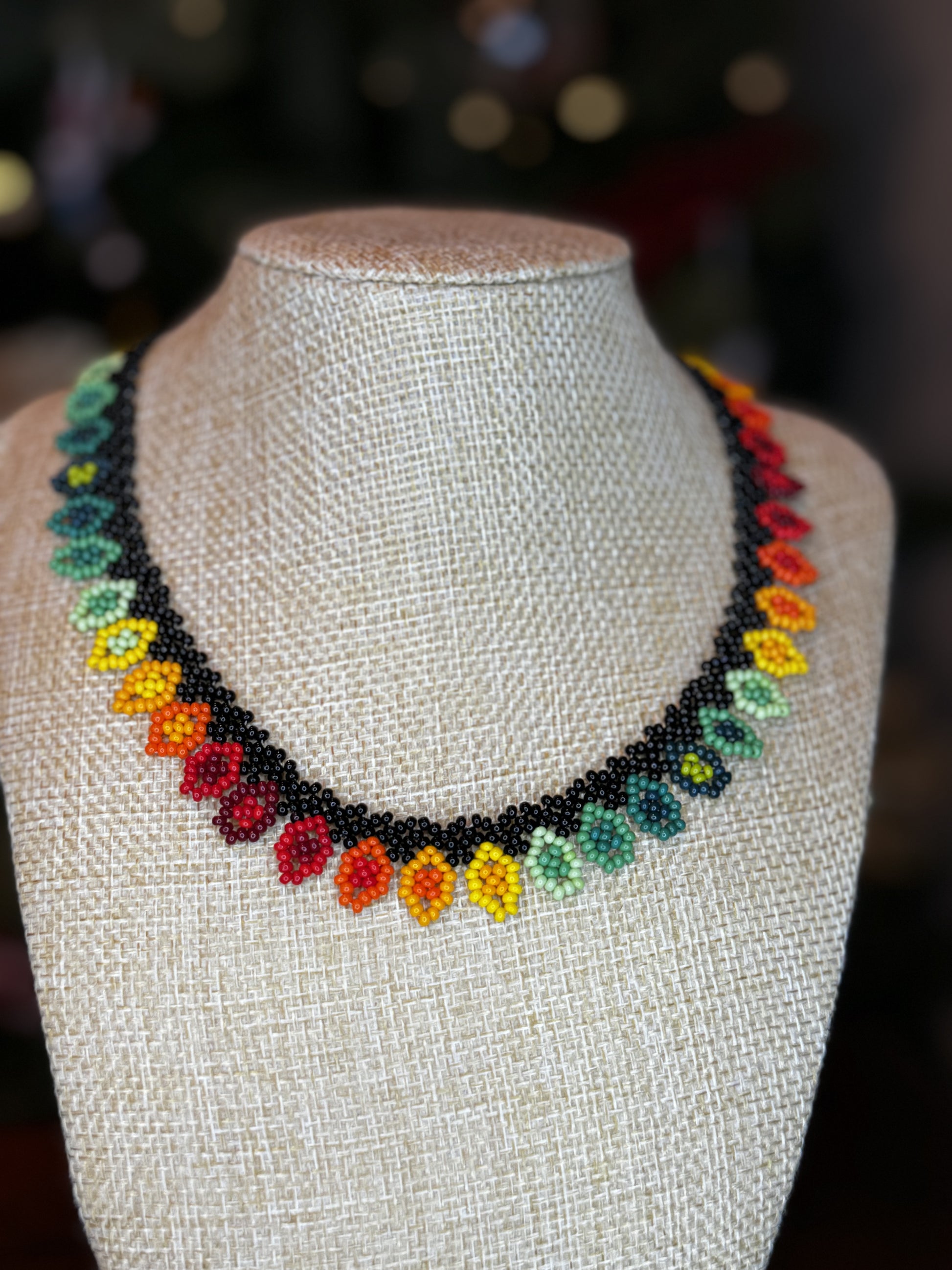 A multicolored beaded necklace with a black border displayed on a mannequin bust.