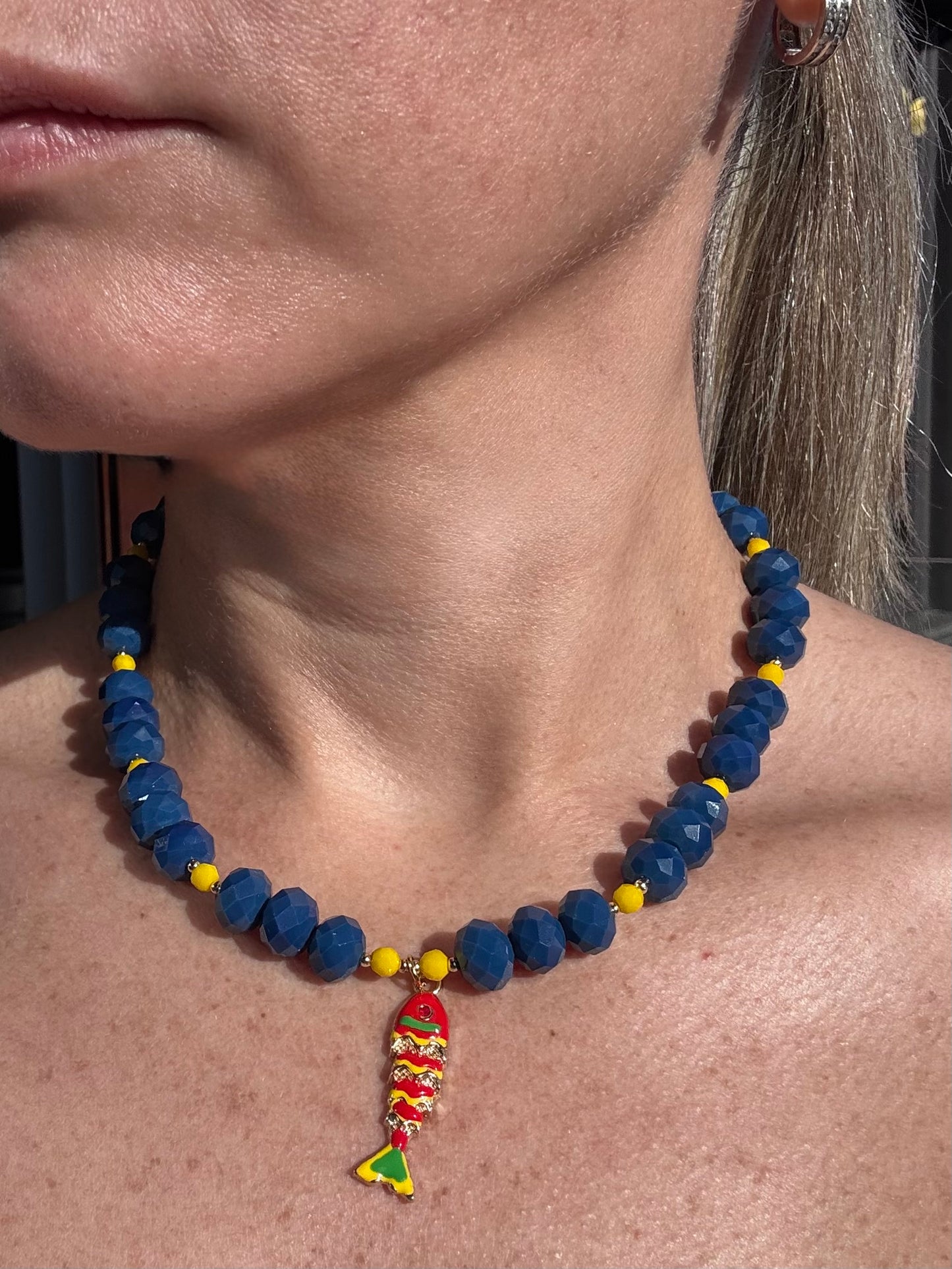 Close-up of a person wearing a blue beaded necklace with a colorful pendant.