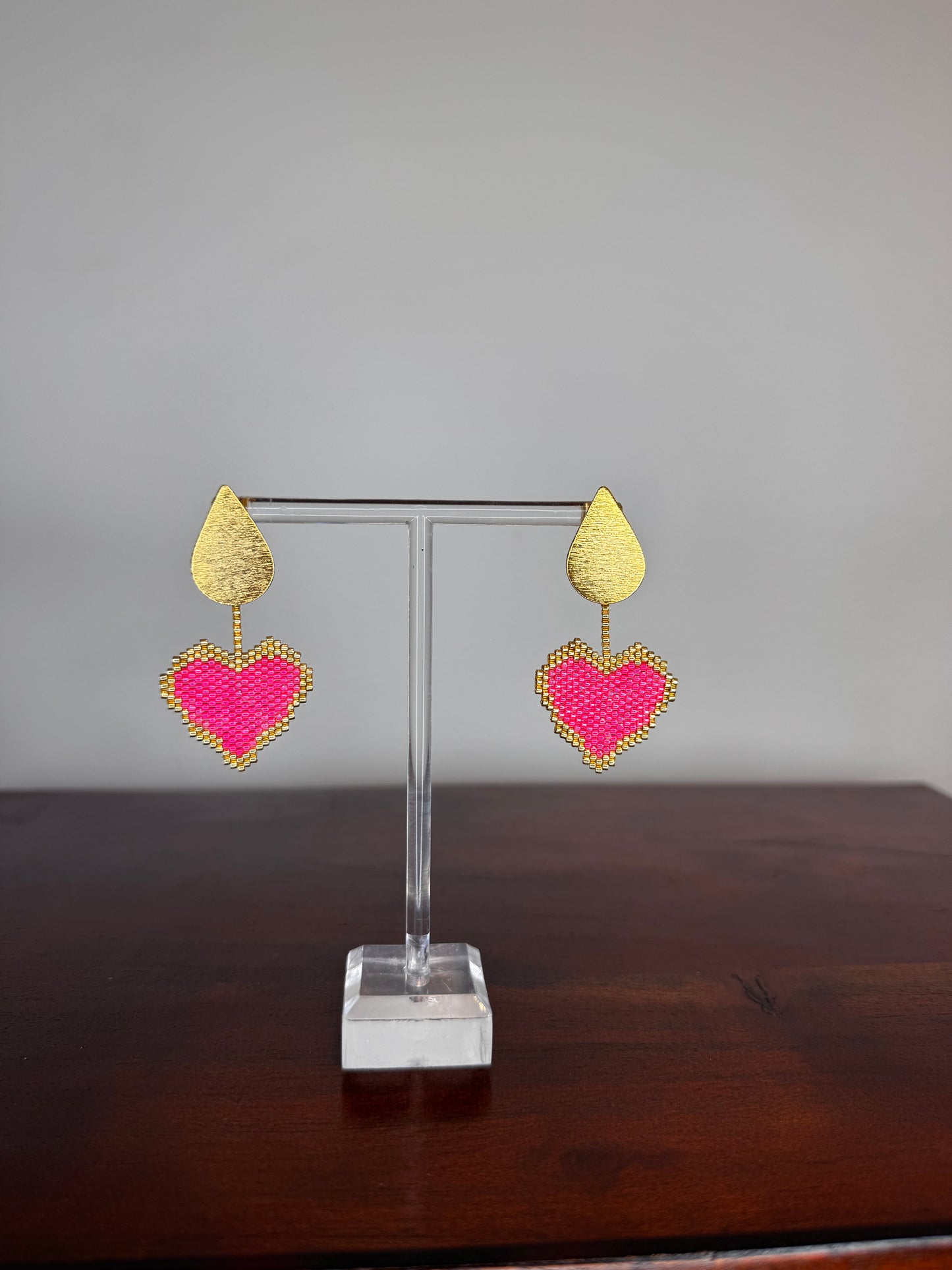 Pair of heart-shaped earrings on a clear stand against a neutral background.