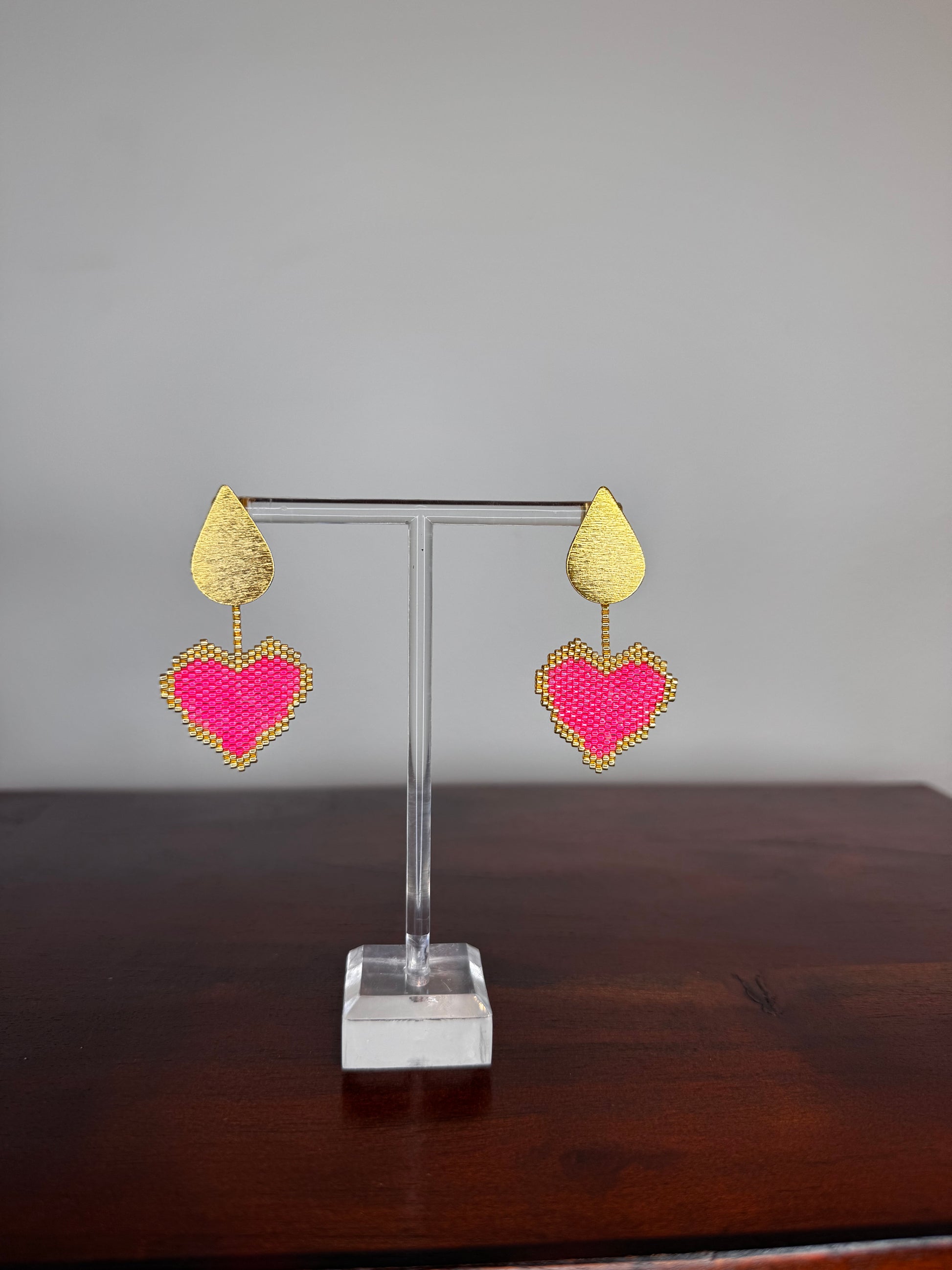 Pair of heart-shaped earrings on a clear stand against a neutral background.