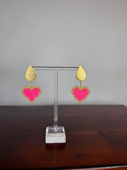 Pair of heart-shaped earrings on a clear stand against a neutral background.