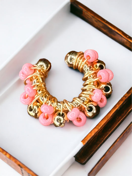 A gold-toned ear cuff with pink and rose gold beads on a white surface.