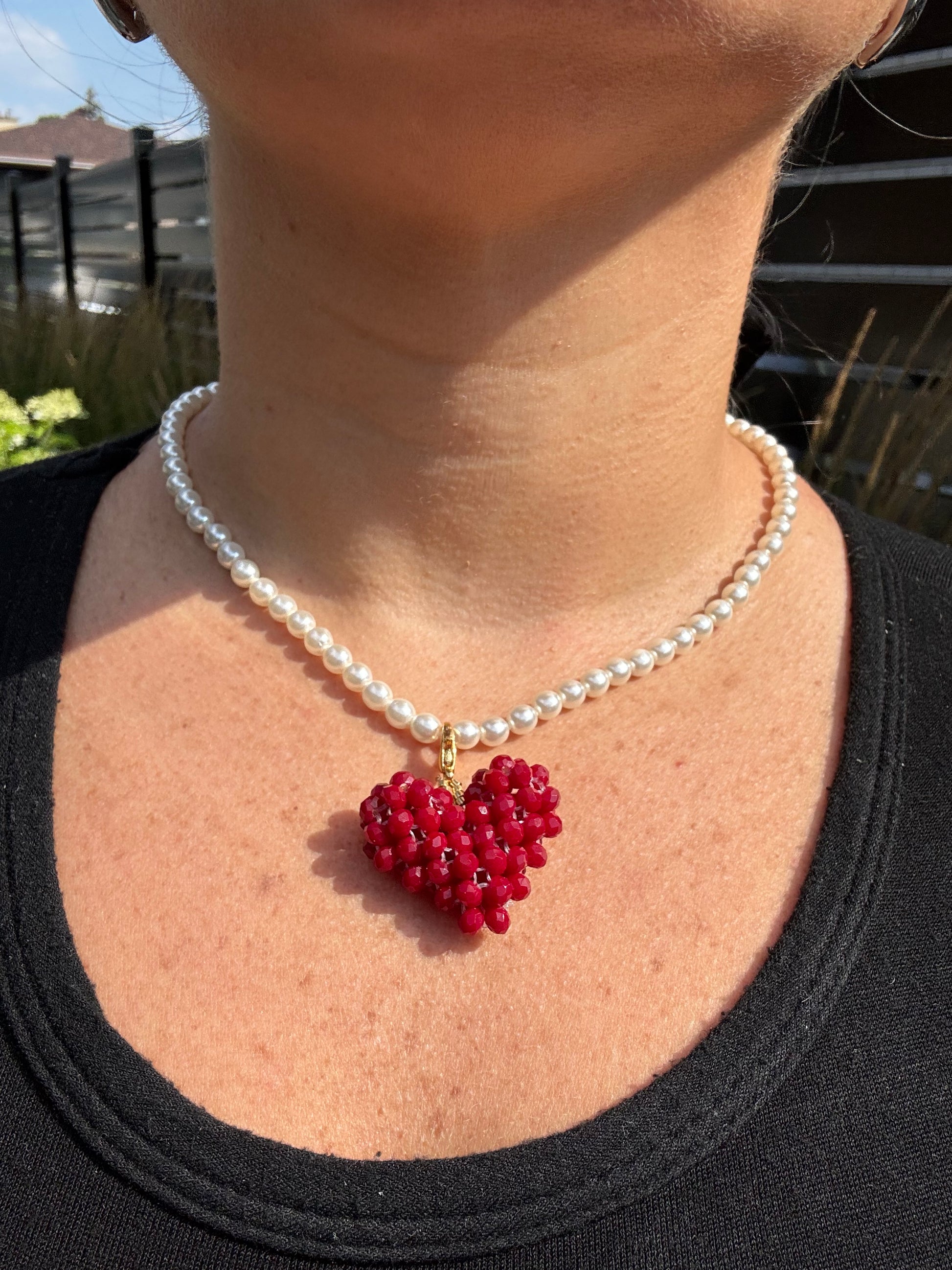 Pearl bracelet with a red flower charm on a person's wrist.