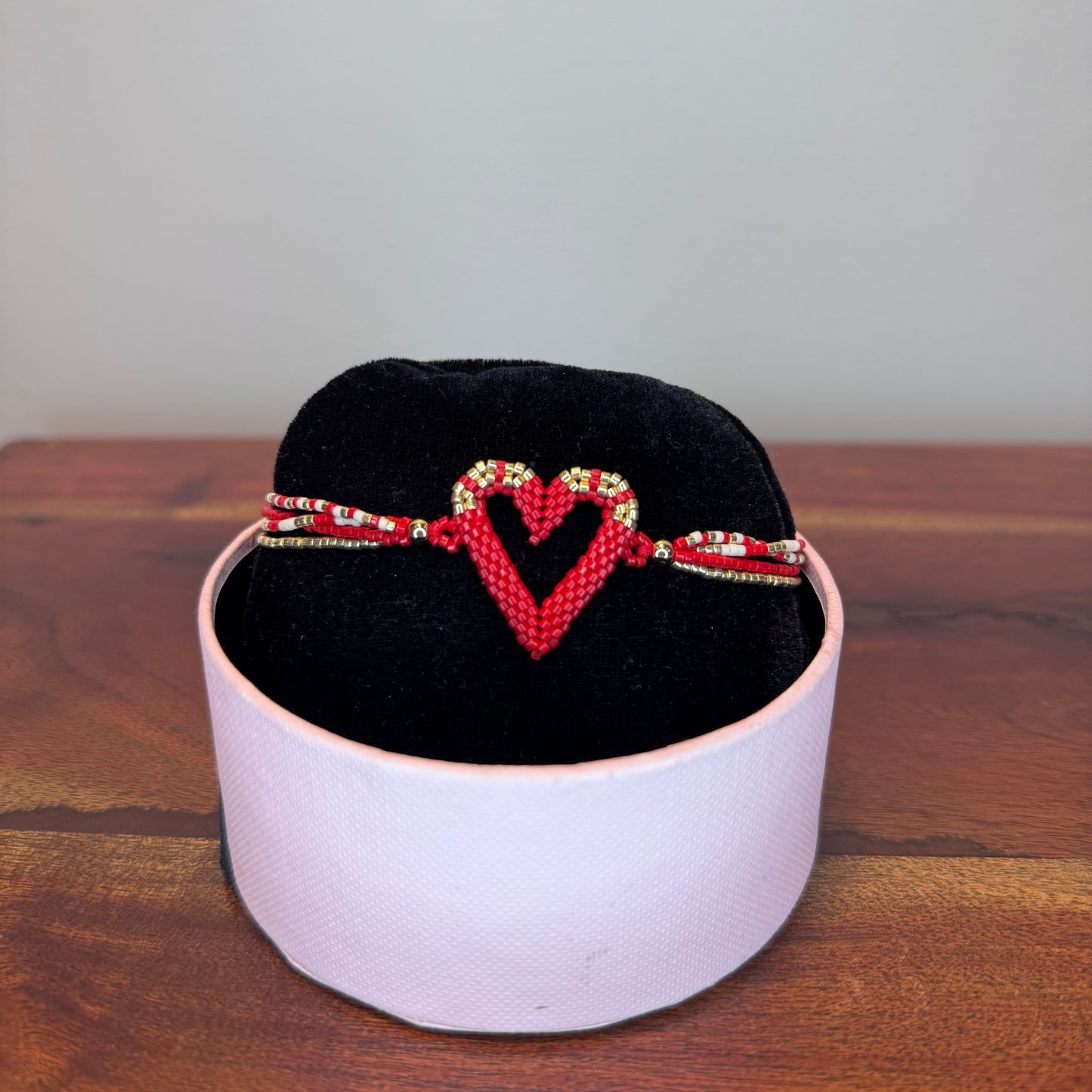 Bracelet with heart design on a black cushion inside a white box on a wooden surface.