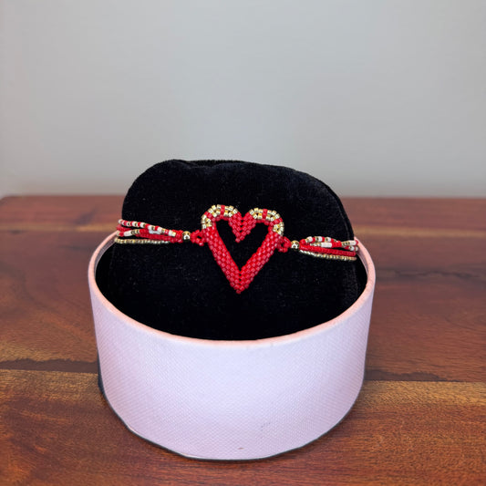 Bracelet with heart design on a black cushion inside a white box on a wooden surface.