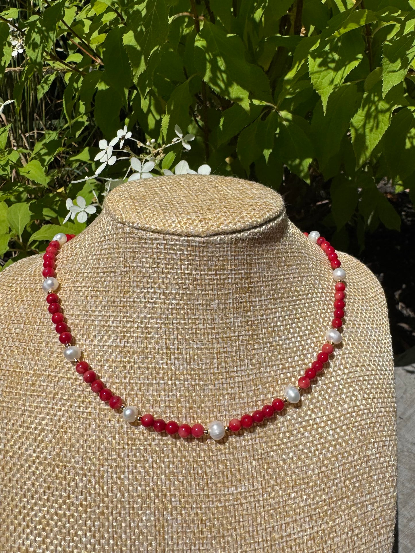Necklace with red and white beads on a mannequin bust against a natural background