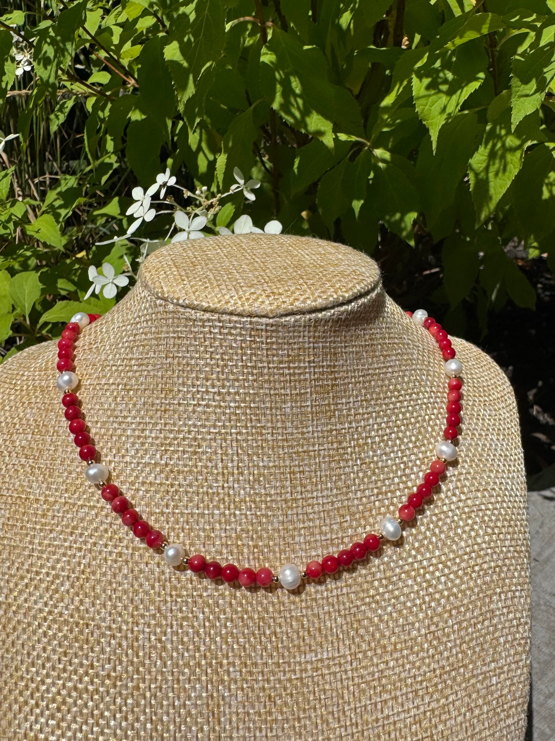 Necklace with red and white beads on a mannequin bust against a natural background