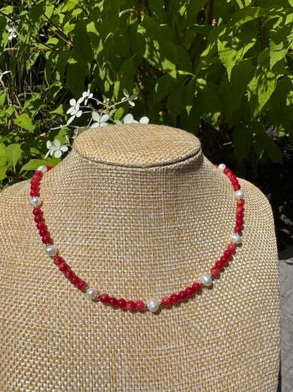 Necklace with red and white beads on a mannequin bust against a natural background