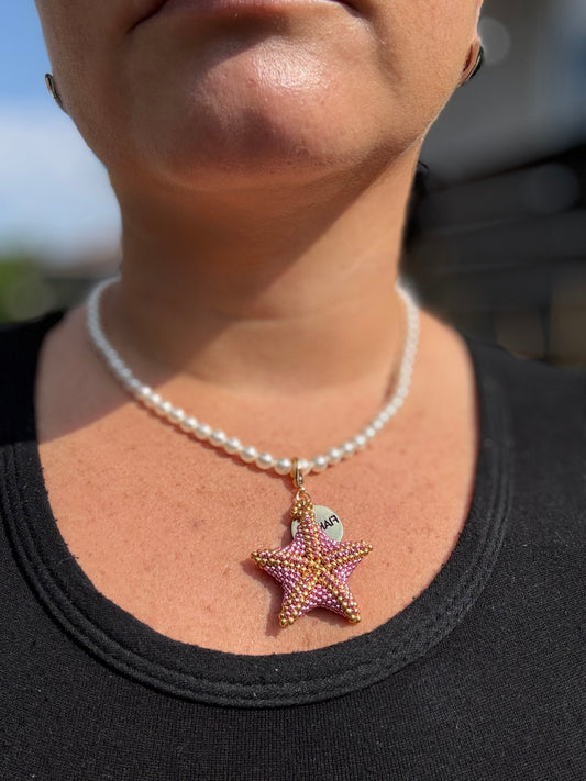 Person wearing a pearl necklace with a starfish pendant outdoors