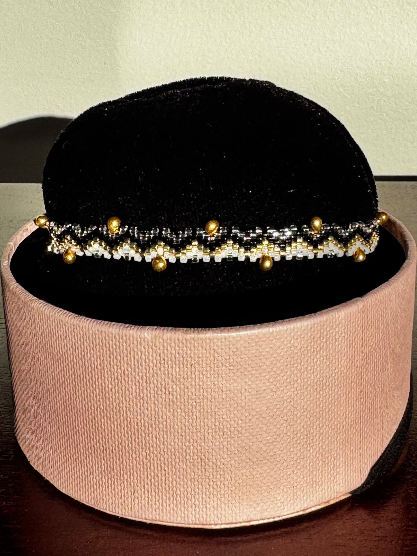 Bracelet with gold beads on a black velvet stand inside a pink box.