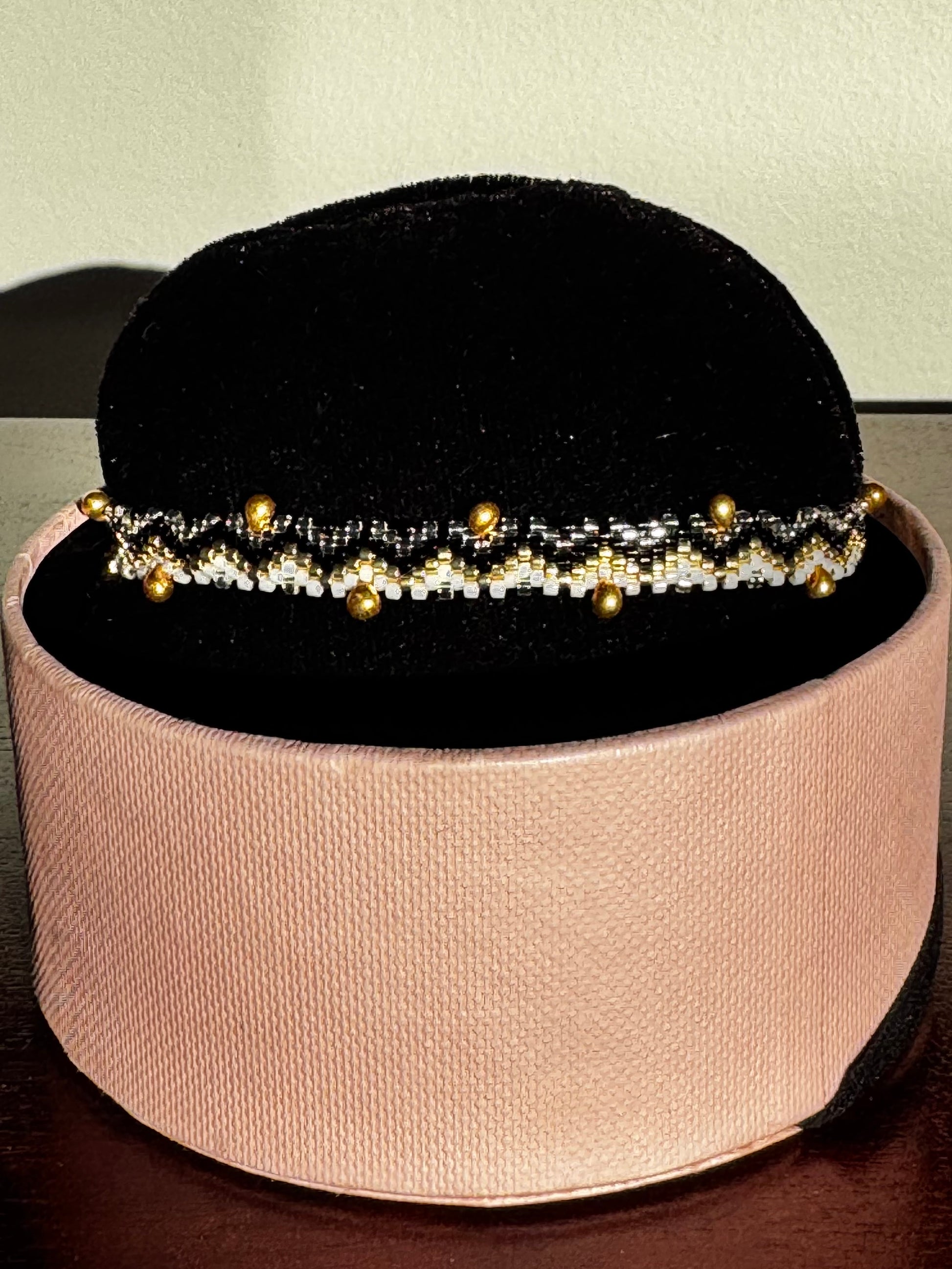 Bracelet with gold beads on a black velvet stand inside a pink box.