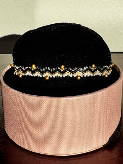 Bracelet with gold beads on a black velvet stand inside a pink box.