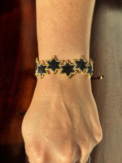 Bracelet with black and gold pattern on a wrist against a neutral background