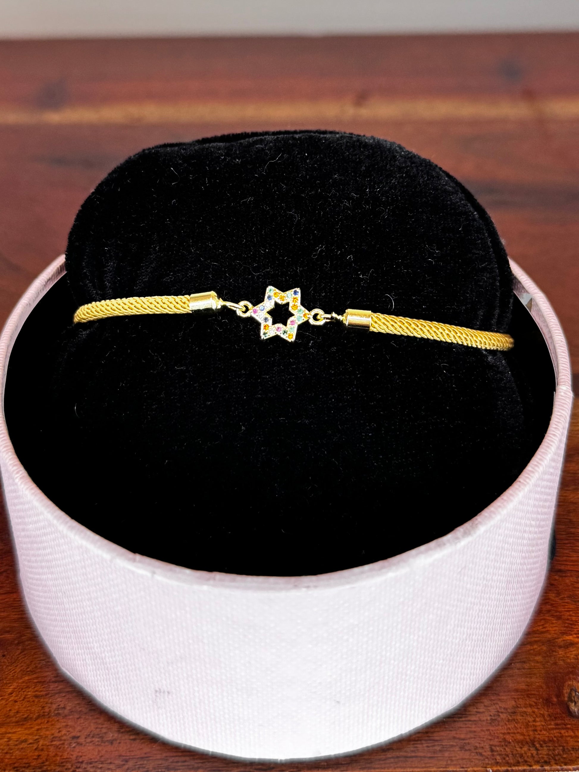 Gold bracelet with a star charm on a black cushion inside a white box on a wooden surface