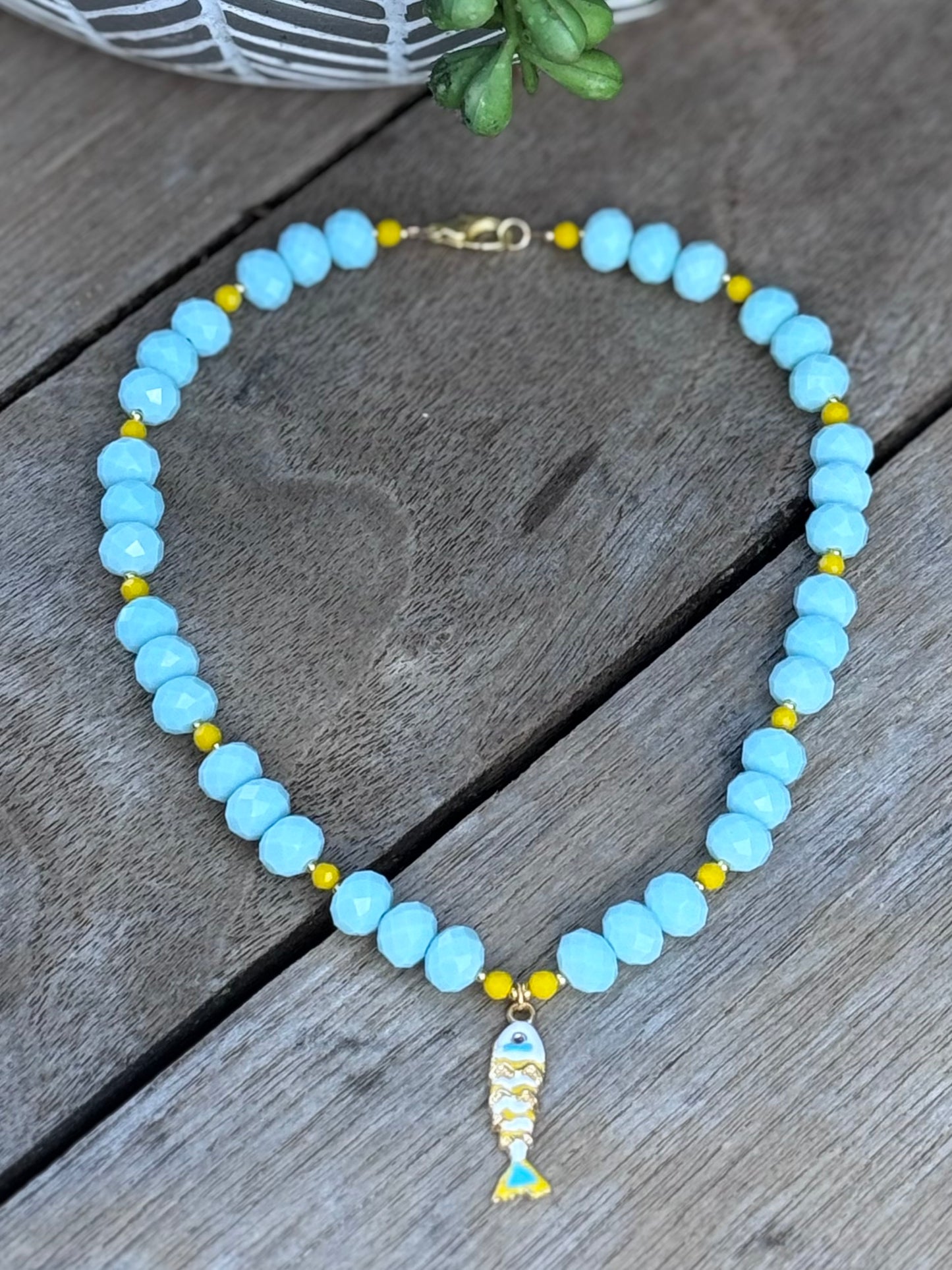 Necklace with blue beads and a fish charm on a wooden surface