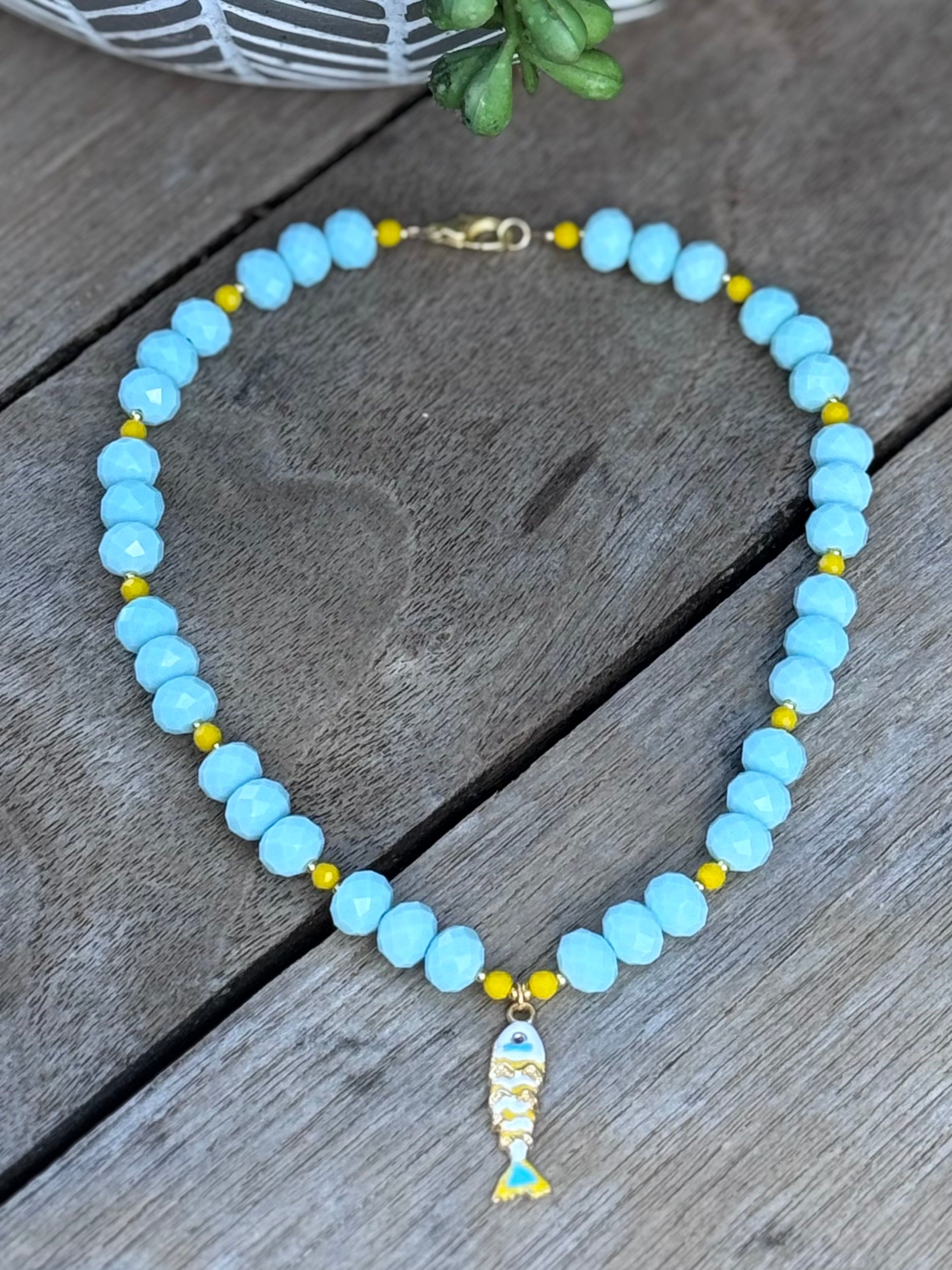 Necklace with blue beads and a fish charm on a wooden surface