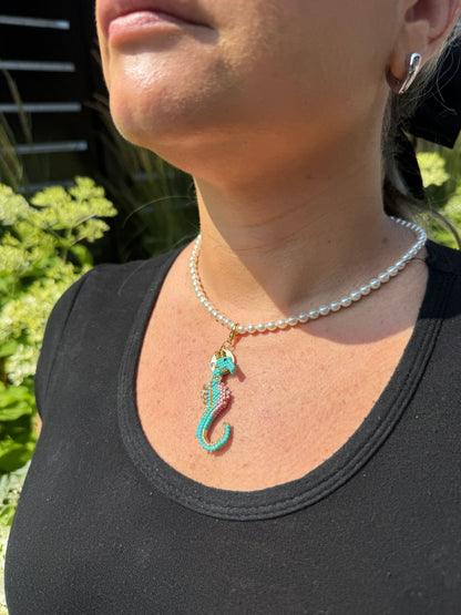 Person wearing a necklace with a seahorse pendant on a black hat with a brown patch.