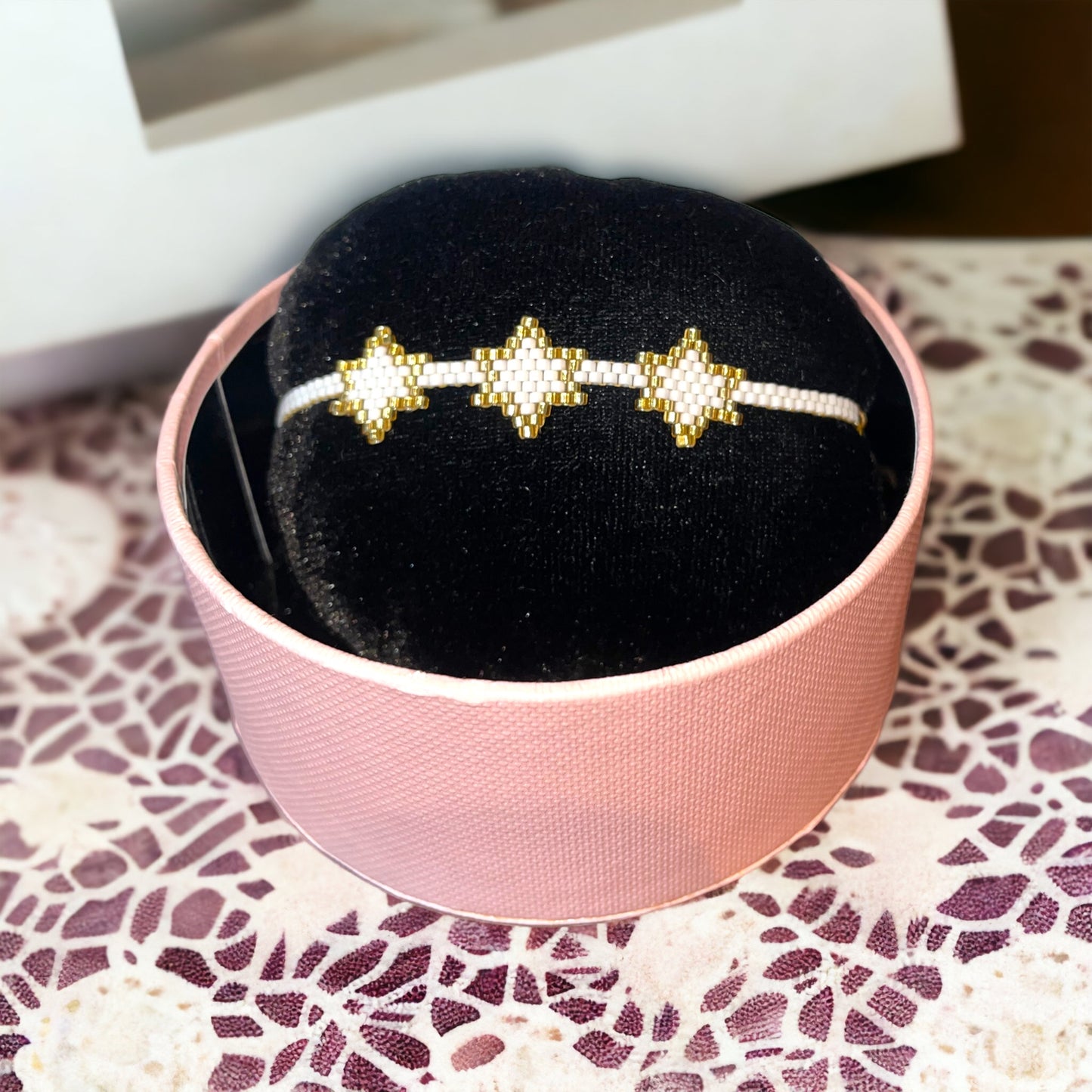 A bracelet with white and gold colors displayed on a black cushion inside a pink box.