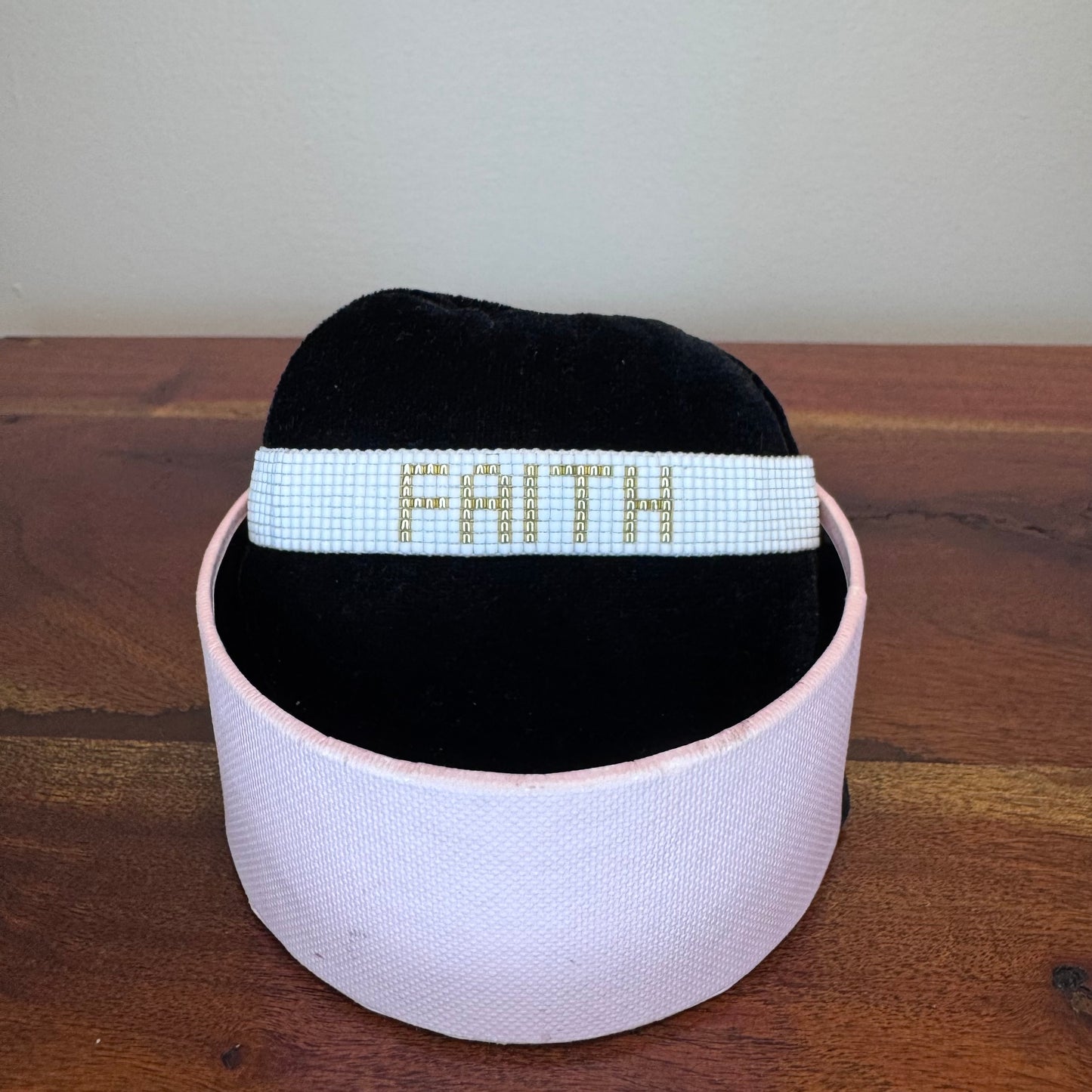 Black headband with 'FAITH' in white beads on a wooden surface