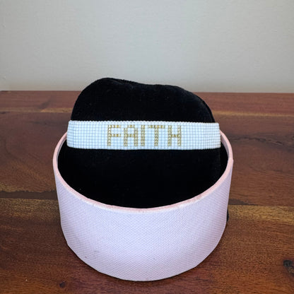 Black headband with 'FAITH' in white beads on a wooden surface