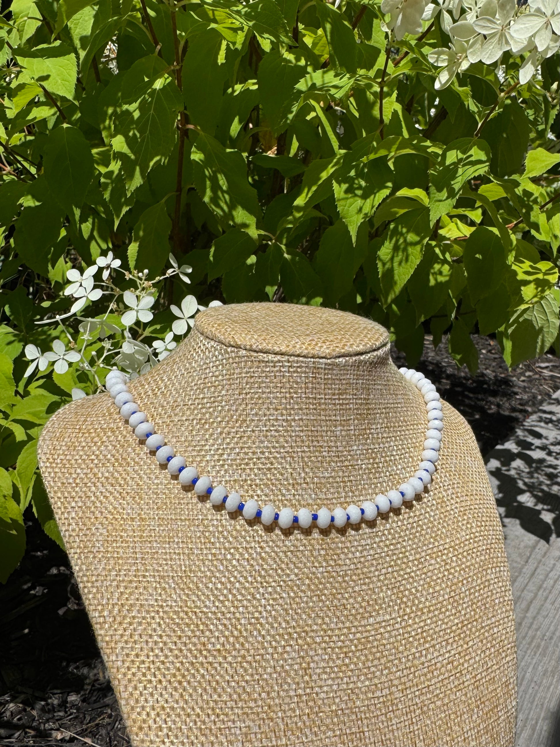 Necklace on a mannequin bust with green foliage in the background