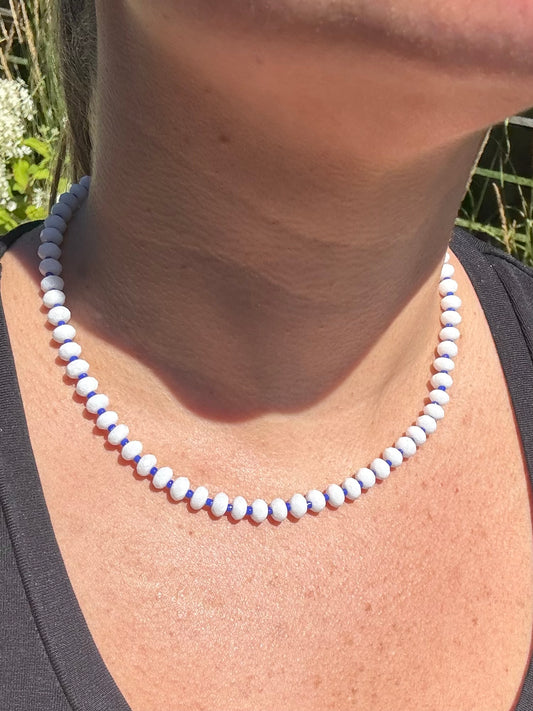 Close-up of a necklace with white and blue beads on a person's neck against a natural background.